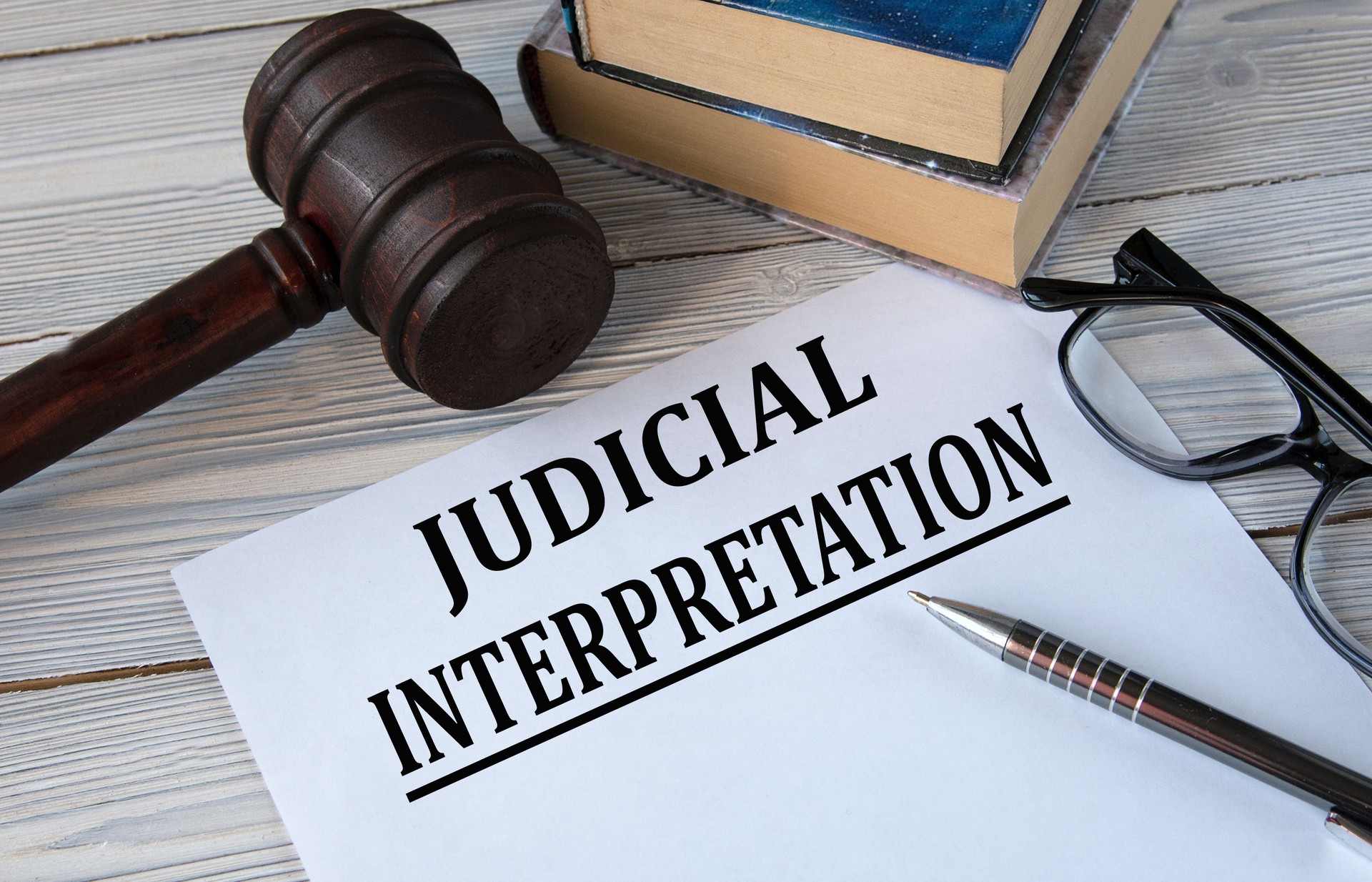 JUDICIAL INTERPRETATION - words on white paper with the background of the judge's hammer, glasses and pen